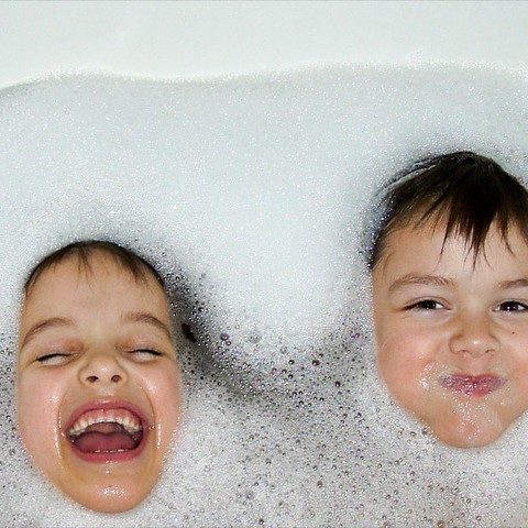 two kids in a bubble bath poke their heads through the bubbles